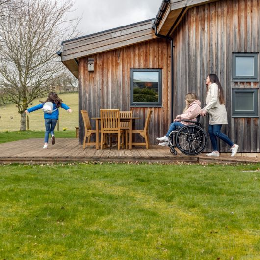 Girl running and girl being pushed in wheelchair at log cabin