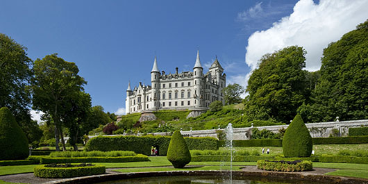 A white turreted castle sits above manicured gardens