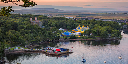 A festival with large marquees sits on a harbour edge