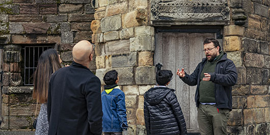 A tour guide speaks to a family in front of a castle door