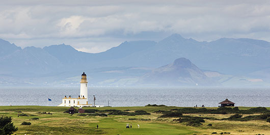 A lighthouse sits on the coastline with mountains on the horizon