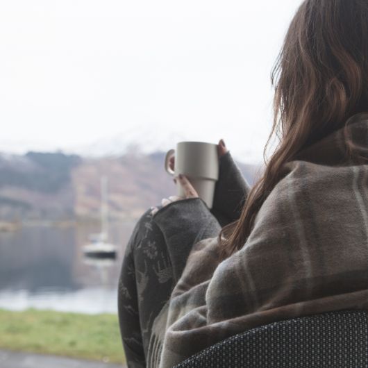 A young lady wrapped up in warm clothing drinks a hot drink as she enjoys the view at the Clachaig Inn, Glencoe