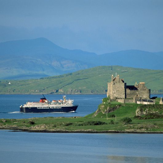 Ferry sailing on sea with mountains in background and castle on an island in foreground