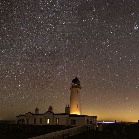 White lighthouse at night with millions of stars in dark sky