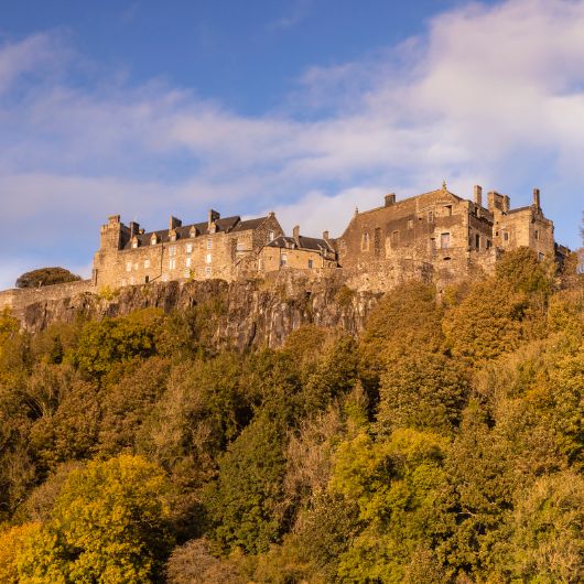 Looking up to Stirling Castle on a hill surrounded by autumnal woodland