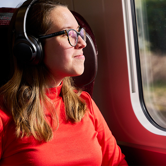 person listening to music on headphones, while looking out of the train window