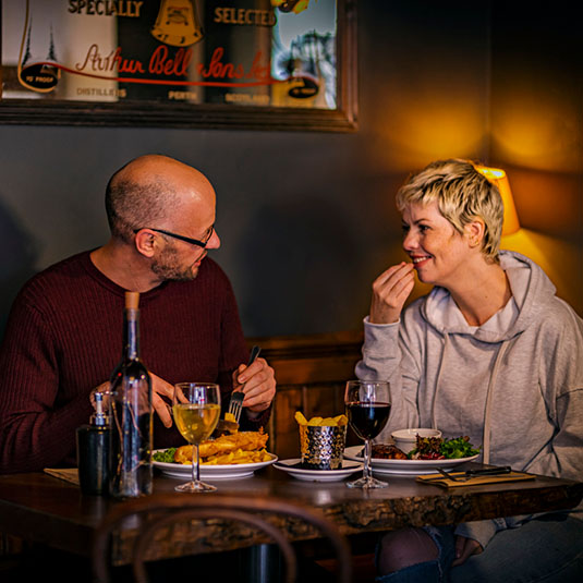 two people enjoying their food and drink at a table in Macgregor's Bar